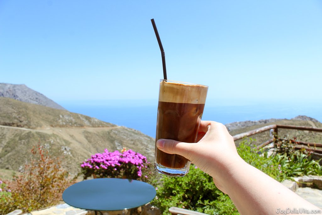 Greek Frappuccino held by one hand over blue water in crete, greece