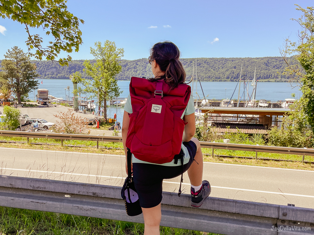 girl with backpack leaning at barrier with lake in the background