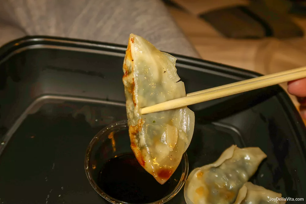 Gyoza held with chopsticks over a black take-out box